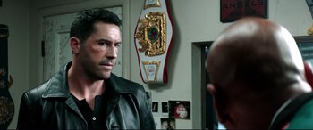 Movie still from “Debt Collectors” (2020), directed by Jesse V. Johnson – A man wearing a black leather jacket in a room; Close Up shot, Over the shoulder angle