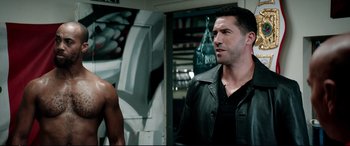 Movie still from “Debt Collectors” (2020), directed by Jesse V. Johnson – A man wearing a leather jacket standing next to a woman; Medium shot, Over the shoulder angle