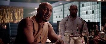 Movie still from “Debt Collectors” (2020), directed by Jesse V. Johnson – A man sitting at a table in front of two bottles; Medium shot, Over the shoulder angle