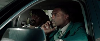 Movie still from “Debt Collectors” (2020), directed by Jesse V. Johnson – Two men sitting in the back of a car talking on a cell phone; Medium shot, Over the shoulder angle