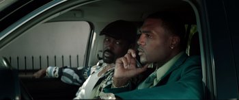 Movie still from “Debt Collectors” (2020), directed by Jesse V. Johnson – Two men sitting in the back of a car talking on a cell phone; Close Up shot, Low angle
