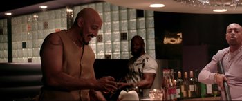 Movie still from “Debt Collectors” (2020), directed by Jesse V. Johnson – Two men sitting at a table in front of a glass wall; Medium shot, Over the shoulder angle