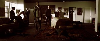 Movie still from “Debt Collectors” (2020), directed by Jesse V. Johnson – A group of men standing around a bed in a dark room; Wide shot, Low angle