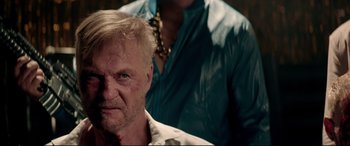 Movie still from “Debt Collectors” (2020), directed by Jesse V. Johnson – An old man with a beard and a chain around his neck; Close Up shot, Over the shoulder angle