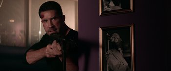 Movie still from “Debt Collectors” (2020), directed by Jesse V. Johnson – A man holding a microphone in front of a picture of a man singing; Medium shot, Over the shoulder angle
