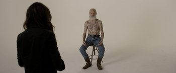 Movie still from “Disobedience” (2017), directed by Sebastián Lelio – An old man with a beard sitting on a stool; Wide shot, High angle