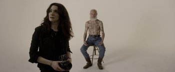 Movie still from “Disobedience” (2017), directed by Sebastián Lelio – A woman taking a picture of a tattooed man; Medium shot, High angle