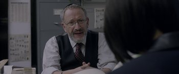Movie still from “Disobedience” (2017), directed by Sebastián Lelio – An older man wearing glasses and a tie talking to a woman; Close Up shot, Over the shoulder angle