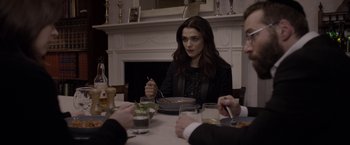 Movie still from “Disobedience” (2017), directed by Sebastián Lelio – A woman sitting at a dinner table with two men; Medium shot, Over the shoulder angle