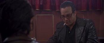 Movie still from “Donnie Brasco” (1997), directed by Mike Newell – A man sitting at a table with a cigarette in his mouth; Close Up shot, Over the shoulder angle