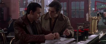 Movie still from “Donnie Brasco” (1997), directed by Mike Newell – Two men sitting at a table looking at a piece of paper; Medium shot, Over the shoulder angle