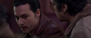 Movie still from “Donnie Brasco” (1997), directed by Mike Newell – A man wearing a brown leather jacket next to another man wearing glasses; Close Up shot, Over the shoulder angle