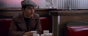 Movie still from “Donnie Brasco” (1997), directed by Mike Newell – A man sitting at a table in front of a plate of food; Close Up shot, Over the shoulder angle