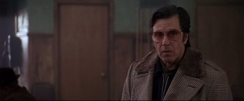 Movie still from “Donnie Brasco” (1997), directed by Mike Newell – A man wearing a coat and glasses in front of a door; Medium shot, Low angle