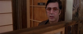 Movie still from “Donnie Brasco” (1997), directed by Mike Newell – A man wearing glasses looking at the camera in front of a wooden wall; Close Up shot, Low angle
