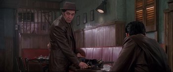 Movie still from “Donnie Brasco” (1997), directed by Mike Newell – A man in a hat and a leather jacket standing in front of a table; Medium shot, Over the shoulder angle