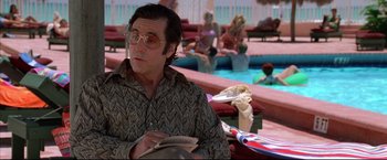 Movie still from “Donnie Brasco” (1997), directed by Mike Newell – A man sitting next to a swimming pool while holding a book; Medium shot, Over the shoulder angle