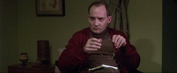 Movie still from “Donnie Brasco” (1997), directed by Mike Newell – A man sitting in a chair holding a pair of glasses; Close Up shot, Over the shoulder angle