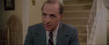 Movie still from “Donnie Brasco” (1997), directed by Mike Newell – A man wearing a suit and tie sitting in front of a staircase; Close Up shot, Low angle