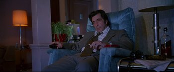 Movie still from “Donnie Brasco” (1997), directed by Mike Newell – A man sitting in a chair smoking a cigarette; Medium shot, Low angle