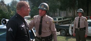 Movie still from “Earthquake” (1974), directed by Mark Robson – A police officer talking to a man on the side of the road; Medium shot, Over the shoulder angle