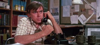 Movie still from “Earthquake” (1974), directed by Mark Robson – A man sitting at a table talking on a phone; Close Up shot, High angle