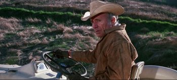 Movie still from “Earthquake” (1974), directed by Mark Robson – An older man wearing a cowboy hat driving a tractor; Medium shot, Over the shoulder angle