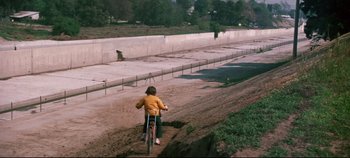 Movie still from “Earthquake” (1974), directed by Mark Robson – A person riding a bike on a dirt road; Extreme Wide shot, High angle