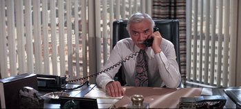 Movie still from “Earthquake” (1974), directed by Mark Robson – An older man sitting at a desk talking on the phone; Medium shot, High angle
