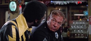 Movie still from “Earthquake” (1974), directed by Mark Robson – A police officer talking to a man sitting next to him; Close Up shot, Over the shoulder angle