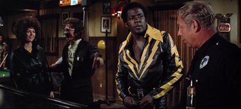 Movie still from “Earthquake” (1974), directed by Mark Robson – A man in a black and yellow jacket standing next to another man in a black and yellow jacket; Medium shot, Over the shoulder angle