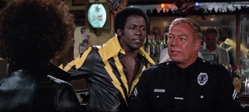 Movie still from “Earthquake” (1974), directed by Mark Robson – A man in a black and yellow jacket standing next to another man in a black and yellow jacket; Medium shot, Over the shoulder angle