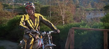 Movie still from “Earthquake” (1974), directed by Mark Robson – A man riding on the back of a yellow motorcycle; Medium shot, Low angle