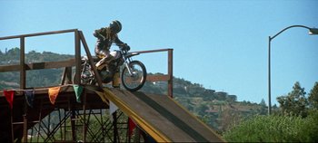Movie still from “Earthquake” (1974), directed by Mark Robson – A man riding a motorcycle down a ramp on top of a hill; Wide shot, Low angle