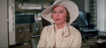 Movie still from “Earthquake” (1974), directed by Mark Robson – An older woman wearing a white hat and a white jacket; Close Up shot, Over the shoulder angle