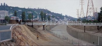 Movie still from “Earthquake” (1974), directed by Mark Robson – A man riding a bike down a dirt road next to a bridge; Extreme Wide shot, High angle