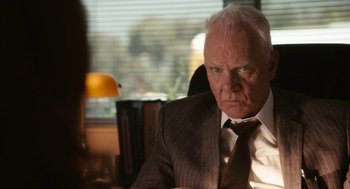 Movie still from “Easy A” (2010), directed by Will Gluck – An older man wearing a suit and tie sitting at a desk; Close Up shot, Over the shoulder angle