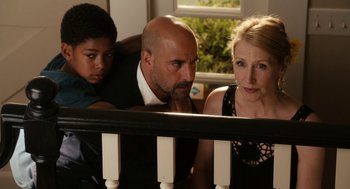 Movie still from “Easy A” (2010), directed by Will Gluck – Two adults and a child looking at something on a table; Medium shot, High angle