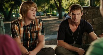 Movie still from “Easy A” (2010), directed by Will Gluck – Two young men sitting next to each other in a park; Medium shot, Over the shoulder angle