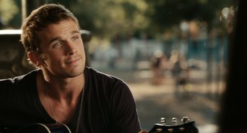 Movie still from “Easy A” (2010), directed by Will Gluck – A man sitting in front of a guitar in a park; Close Up shot, Over the shoulder angle