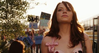 Movie still from “Easy A” (2010), directed by Will Gluck – A woman in a pink dress is standing in front of a group of people; Close Up shot, Over the shoulder angle
