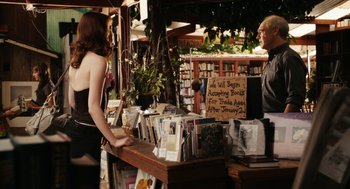 Movie still from “Easy A” (2010), directed by Will Gluck – A woman standing in front of a table of books; Medium shot, Over the shoulder angle