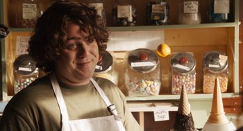 Movie still from “Easy A” (2010), directed by Will Gluck – A man in an apron standing in front of a display of candy; Close Up shot, Over the shoulder angle