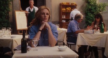 Movie still from “Eat Pray Love” (2010), directed by Ryan Murphy – A woman sitting at a table with a glass of wine in front of her; Medium shot, Over the shoulder angle