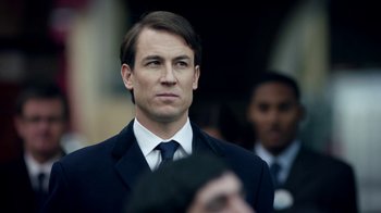 Movie still from “Black Mirror” (2011), created by Charlie Brooker – A man in a suit and tie looking at something; Close Up shot, Over the shoulder angle