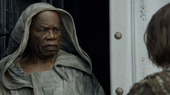 Movie still from “Game of Thrones” (2011), created by D.B. Weiss – An old man in a hooded robe is standing next to a metal pole; Close Up shot, Low angle