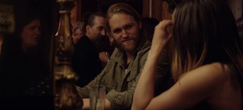 Movie still from “Black Mirror” (2011), created by Charlie Brooker – A man with long hair sitting at a table with other people; Close Up shot, Over the shoulder angle