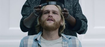 Movie still from “Black Mirror” (2011), created by Charlie Brooker – A man with a beard is getting his head shaved by another man; Close Up shot, Overhead angle