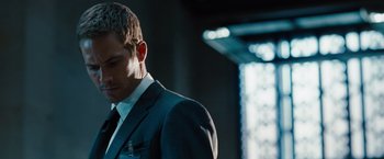 Movie still from “Fast & Furious” (2009), directed by Justin Lin – A man wearing a suit and tie standing in a room; Close Up shot, Over the shoulder angle