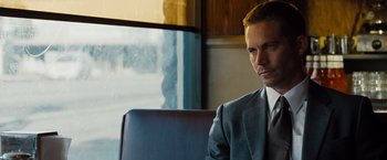 Movie still from “Fast & Furious” (2009), directed by Justin Lin – A man in a suit and tie sitting in a chair in front of a window; Close Up shot, Over the shoulder angle